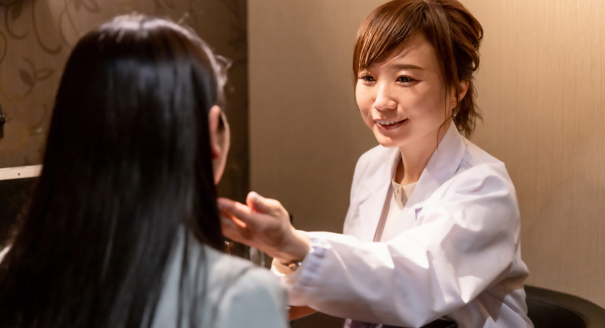 女性医師が女性の顔に手を添えて笑顔で診断をしている